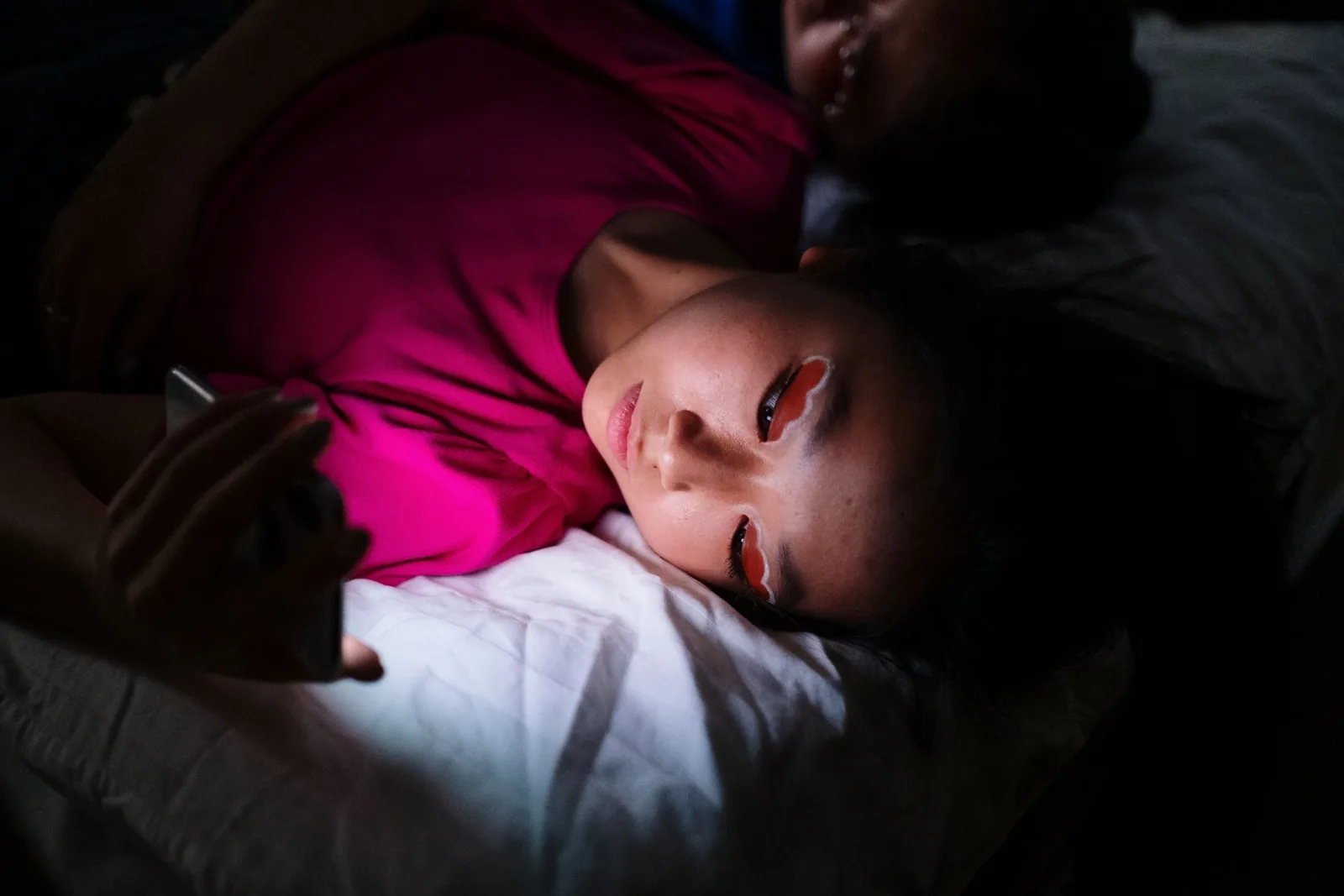 A creator lying in bed at night, face lit by her phone, replying to messages