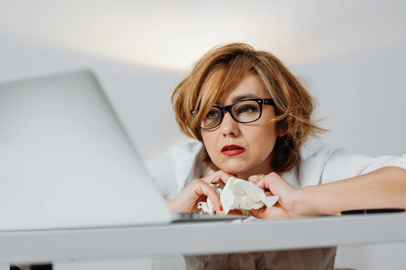 A creator at a desk looking stressed with crumpled paper drafts around the laptop